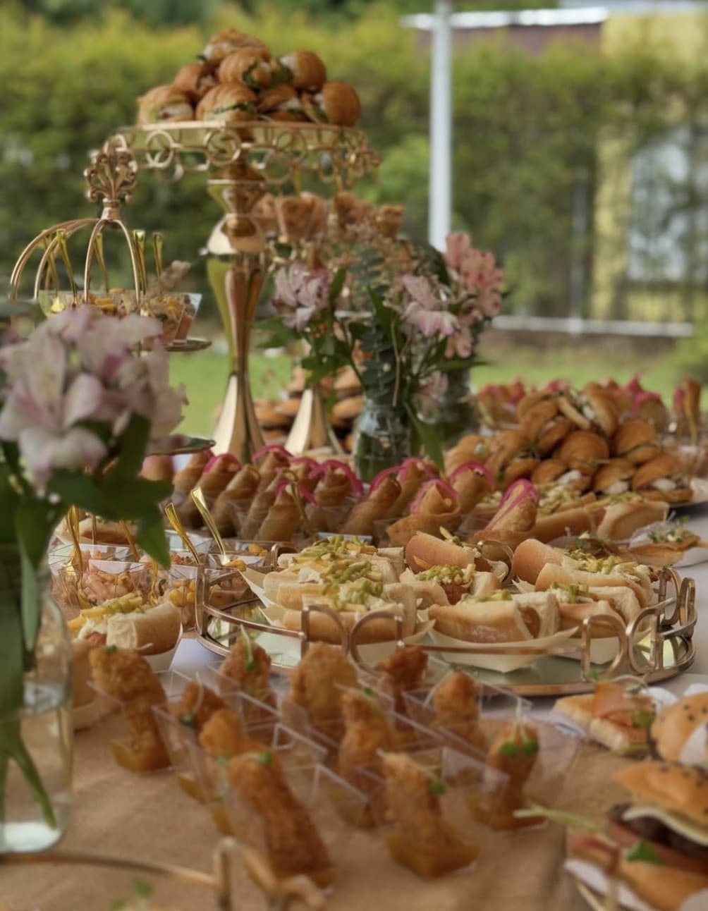 Mesa de pasabocas en un jardín, con flores y bases doradas